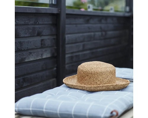 Stråhatt på rutig kudde framför trävägg