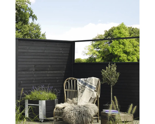 Dekorativ trädgårdsscen med trästaket, planteringskärl, rottingfåtölj och växter