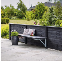 Trädgårdsscen med träbänk mot trästaket, prydnadskuddar, dryck och blomkruka.