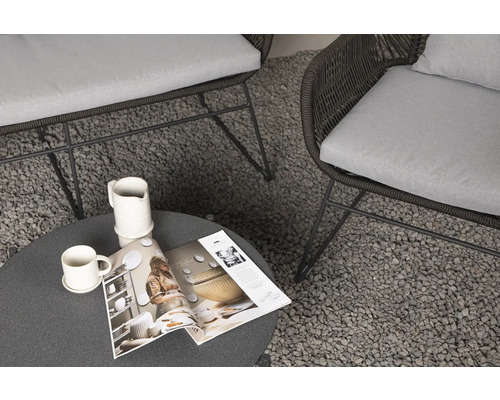 Scen med två fåtöljer med kuddar, ett runt bord, kopp, kanna och en tidning