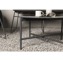 Detaljvy av ett grått soffbord med stålram, på ett grusgolv, med koppar och en tidning på bordsskivan.