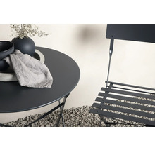 Trädgårdsscen med bistrobord, stol, porslin och duk utomhus.