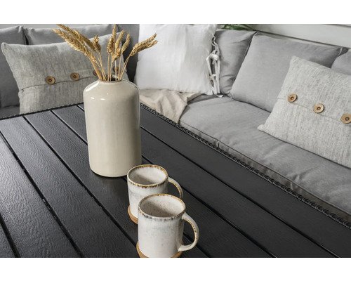 Trädgårdsbord med två koppar, en vas med veteax och kuddar på en bänk