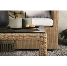 Närbild av ett rottingbord med glasskiva, dekoration och en rottingfåtölj i bakgrunden