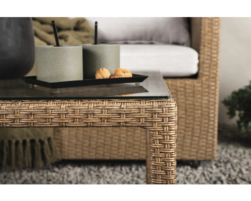 Närbild av ett rottingbord med glasskiva, dekoration och en rottingfåtölj i bakgrunden