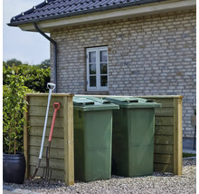 Två gröna soptunnor med träkant och trädgårdsredskap framför en tegelbyggnad.