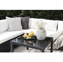 Trädgårdssoffa med kuddar, bord med glasskiva, fruktskål och dekoration utomhus.