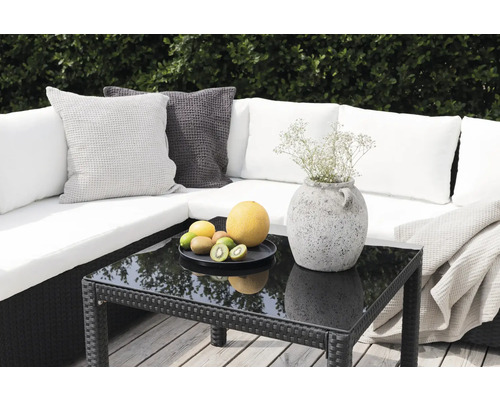 Trädgårdssoffa med kuddar, bord med glasskiva, fruktskål och dekoration utomhus.