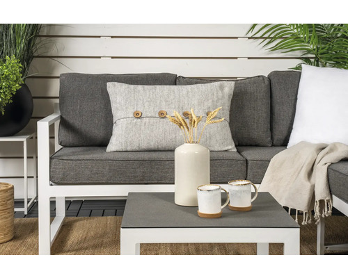 Trädgårdsscen med soffa, kudde med knappar, bord, vas, koppar och dekoration