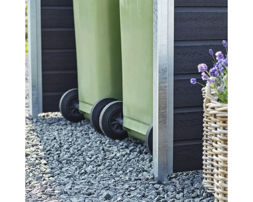 Två gröna soptunnor i ett soptunneskydd på grus