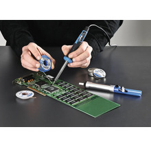 Person löder ett kretskort med en lödkolv, lödtenn och avlödningspump.