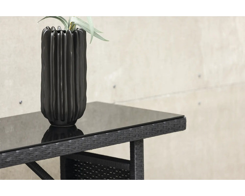 Närbild av ett trädgårdsbord med glasskiva och en vas