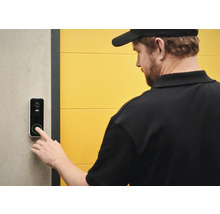 En person trycker på en dörrklocka med kamerafunktion.