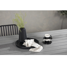 Dekorativt stilleben med vas, växt, porslin och textilier på ett trädgårdsbord.