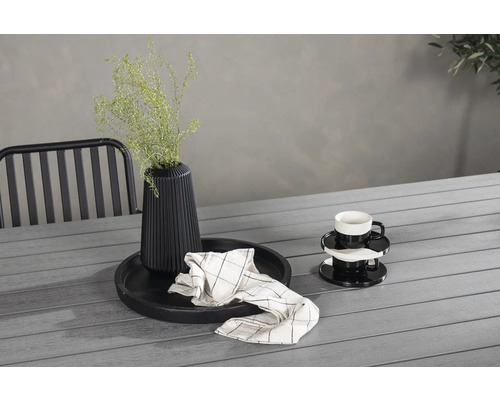 Dekorativt stilleben med vas, växt, porslin och textilier på ett trädgårdsbord.