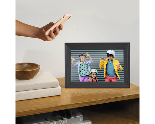 Digital fotoram på en trähylla med ett foto av tre barn och en hand som håller i en smartphone