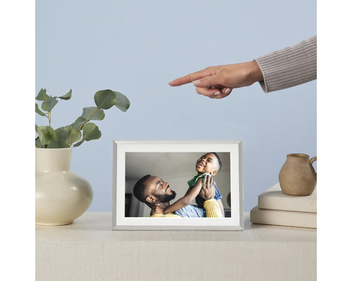 Digital fotoram med foto av en far och hans son på ett bord, bredvid en vas med eukalyptus och en hand som pekar på ramen.