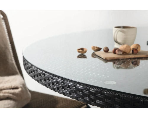 Detaljbild av ett runt trädgårdsbord med glasskiva och rottingkant.