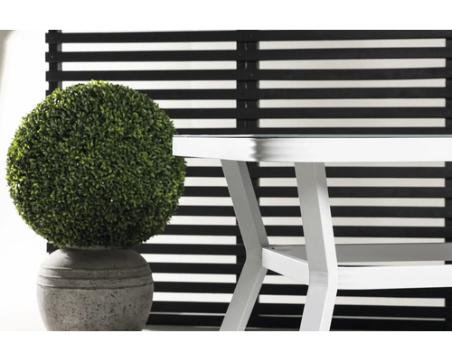 Dekorativ grön konstgjord växt i kruka bredvid ett vitt bord