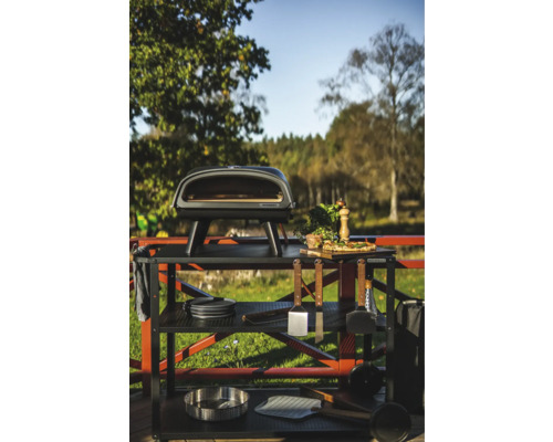 Utekök med pizzaugn, grillverktyg och tillbehör på ett robust metallbord utomhus