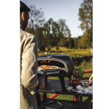 Man skjuter in pizza med pizzaspade i pizzaugn i trädgården.