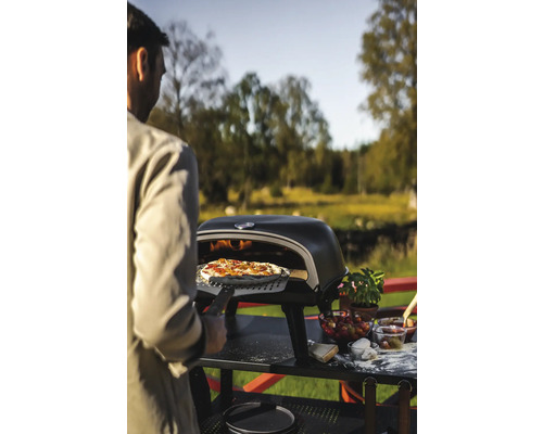 Man skjuter in pizza med pizzaspade i pizzaugn i trädgården.