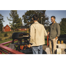 Utomhusscen med två män bredvid en svart pizzaugn som lagar pizza