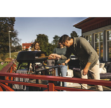 Person skjuter in pizza i en pizzaugn utomhus medan två andra personer tittar på