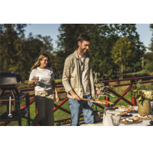 En utomhusscen med människor som lagar och serverar pizza, med en grill och ett bord