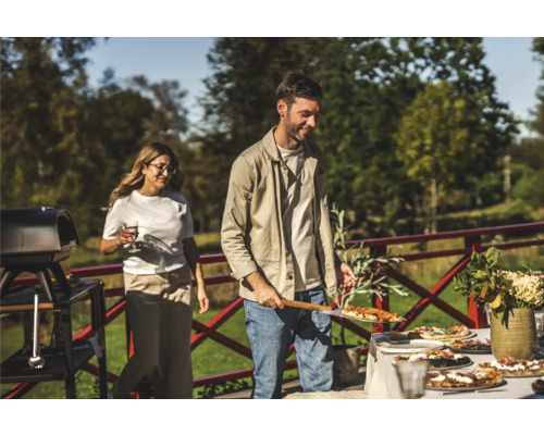 En utomhusscen med människor som lagar och serverar pizza, med en grill och ett bord