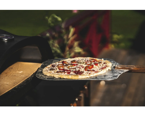 Pizza på pizzaspade framför pizzaugn