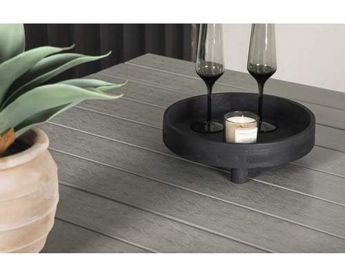 Dekorativt arrangemang med växt, ljus och glas på ett trädgårdsbord.