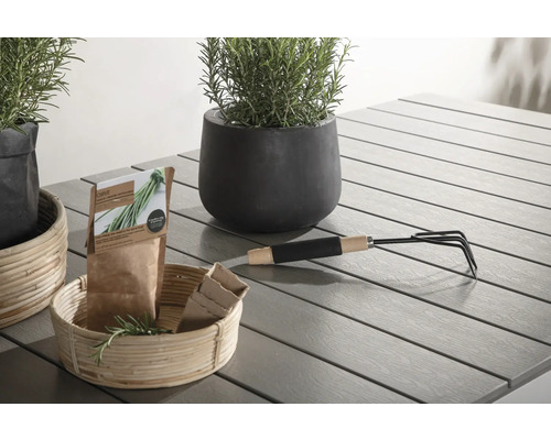 Scen med planteringskärl, örter, trädgårdsredskap och fröpåsar på ett trädgårdsbord.