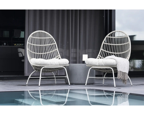 Två rottingfåtöljer med kuddar och ett sidobord på en terrass intill en pool