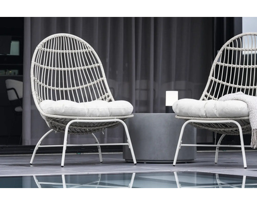 Två rottingfåtöljer med sittdynor och ett bord utomhus.