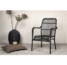 Dekorativ scen med en svart rottingfåtölj, en kudde, en kopp och en vas med torkade blommor.