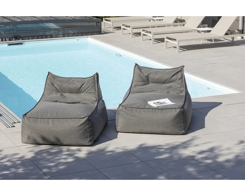 Två grå sittpuffar i tyg står på en terrass bredvid en pool.