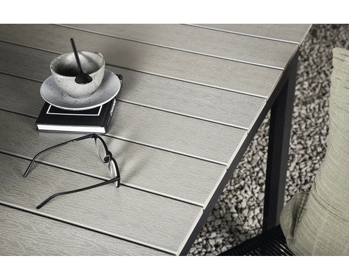 Närbild av ett trädgårdsbord med bok, kopp, glasögon och kudde