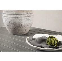 Dekorativt arrangemang med kruka, tallrik, tygservett och kronärtskocka på ett bord