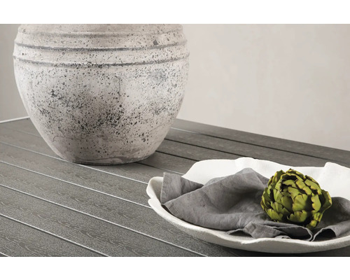 Dekorativt arrangemang med kruka, tallrik, tygservett och kronärtskocka på ett bord