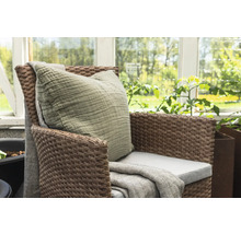 Flätad fåtölj med kudde och filt i trädgården