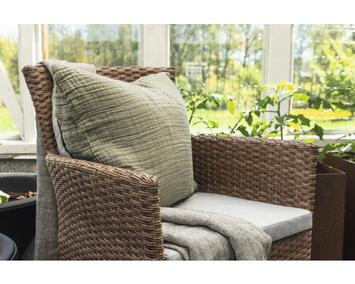 Flätad fåtölj med kudde och filt i trädgården