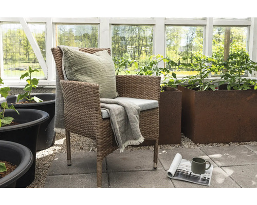 Trädgårdsscen med rottingfåtölj, kudde och blomlådor i växthuset