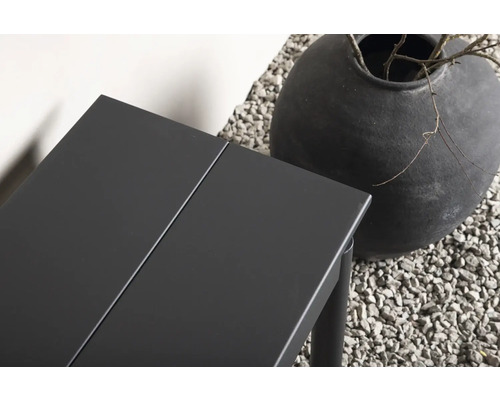 Detalj av ett trädgårdsbord i metall bredvid en stor vas på grus