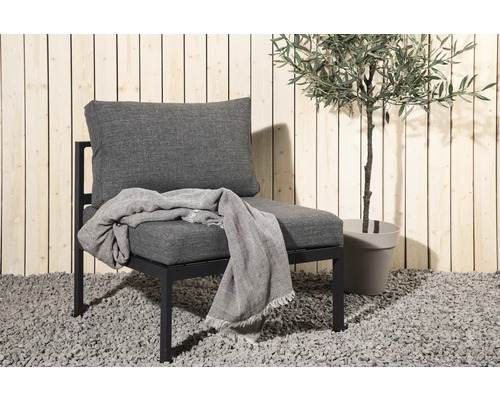 Trädgårdsfåtölj med kudde och filt bredvid ett olivträd i kruka.