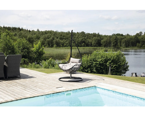 Scen med en hängande metallstol med kuddar på en träterrass bredvid en pool med utsikt över en sjö