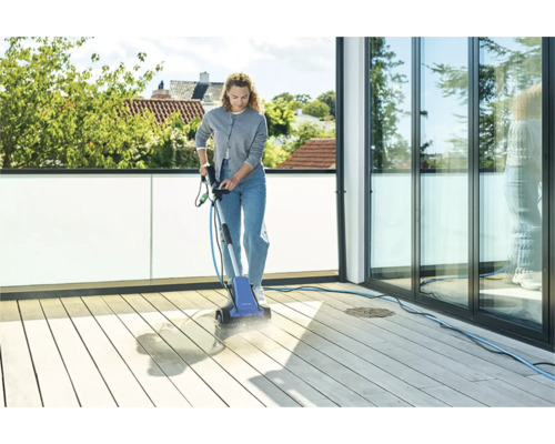 En kvinna rengör en träterrass med en elektrisk terrasstvätt.