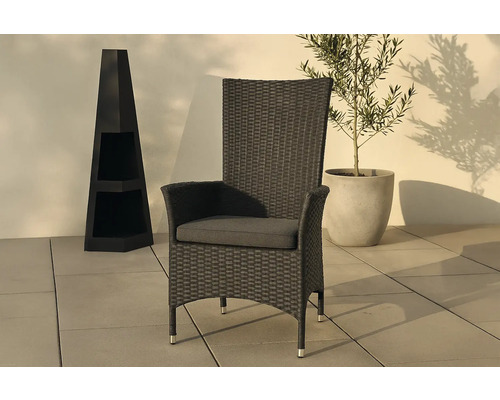 Flätad trädgårdsfåtölj med armstöd och sittdyna bredvid en dekorativ kolonn och en krukväxt.