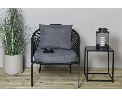 Miljö med en svart utomhusfåtölj med kuddar, ett sidobord med lykta och en krukväxt.