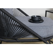 Detaljvy av en stol med flätat ryggstöd och en grå sittdyna med en kopp och ett fat ovanpå.